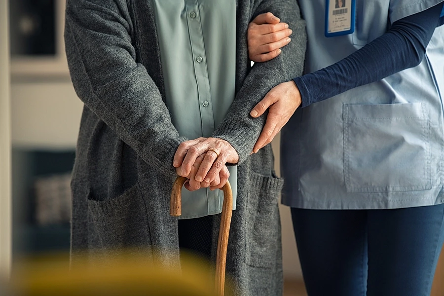 Nurse assisting older patient with walking stick